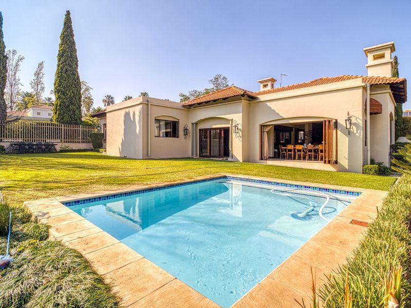 A well-maintained rear garden featuring a swimming pool with tiled surround, leading to an open-plan living area through large bi-fold doors.