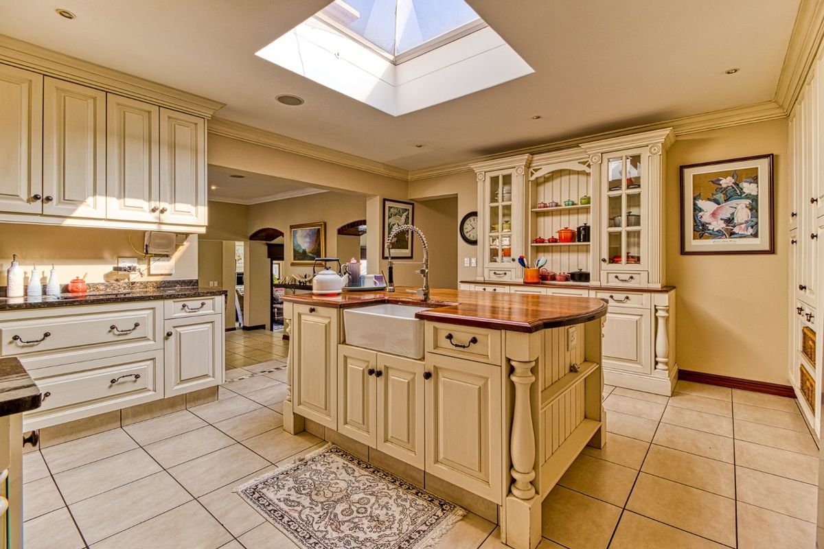 A spacious, well-lit kitchen featuring a central island with a farmhouse sink, ample built-in cabinetry, and a large skylight.