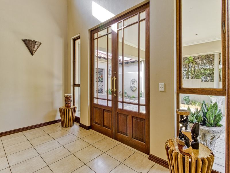 Welcoming entrance hall featuring double timber-framed glass doors, tiled flooring, and natural light flowing through adjacent sidelight windows.