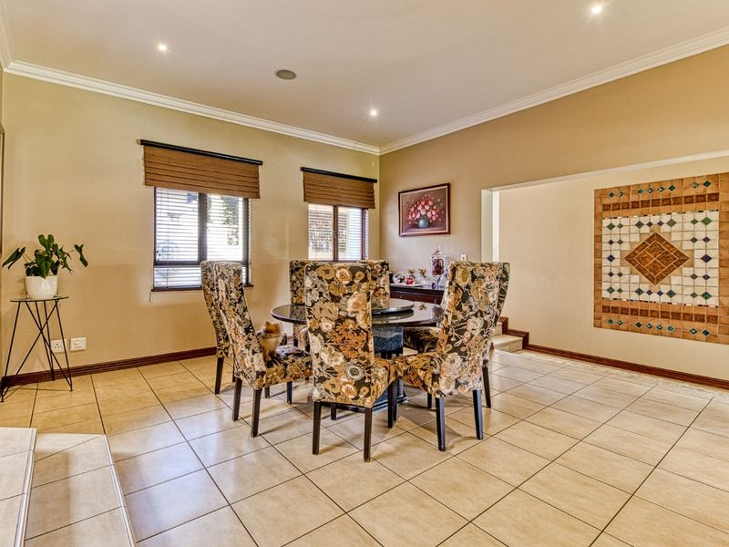 A spacious dining room featuring neutral ceramic floor tiles, recessed lighting, and a decorative tiled wall feature, offering a functional and well-lit living space.