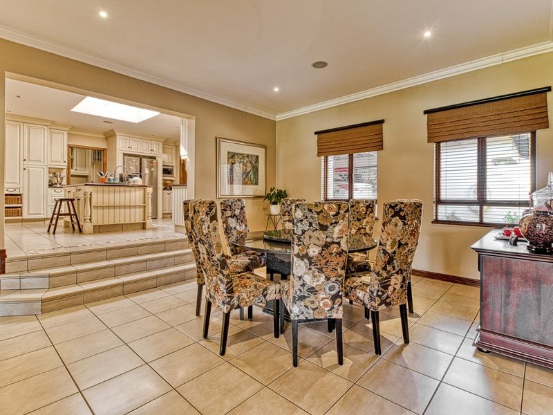 Open-plan dining area featuring tiled floors and crown molding, with a step-up transition into a spacious kitchen equipped with built-in cabinetry and a central island.