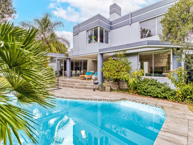 Rear view of a two-story house featuring a swimming pool, stone-paved patio area, and large sliding glass doors leading to the interior living space.