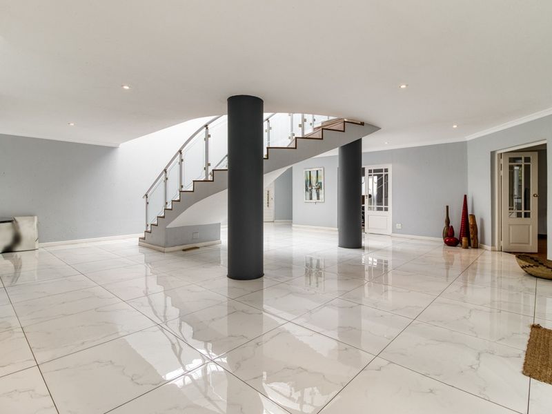 Spacious entrance hall featuring a striking curved staircase with glass balustrade, polished porcelain floor tiles, and modern structural columns.