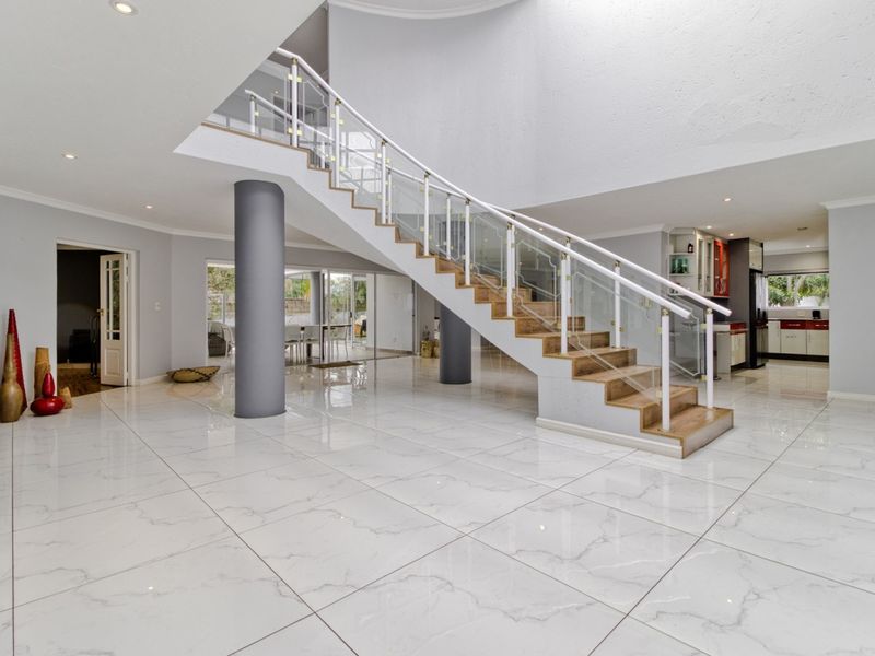 Spacious double-volume entrance hall featuring a modern staircase with glass balustrades, polished marble-look floor tiles, and recessed lighting.