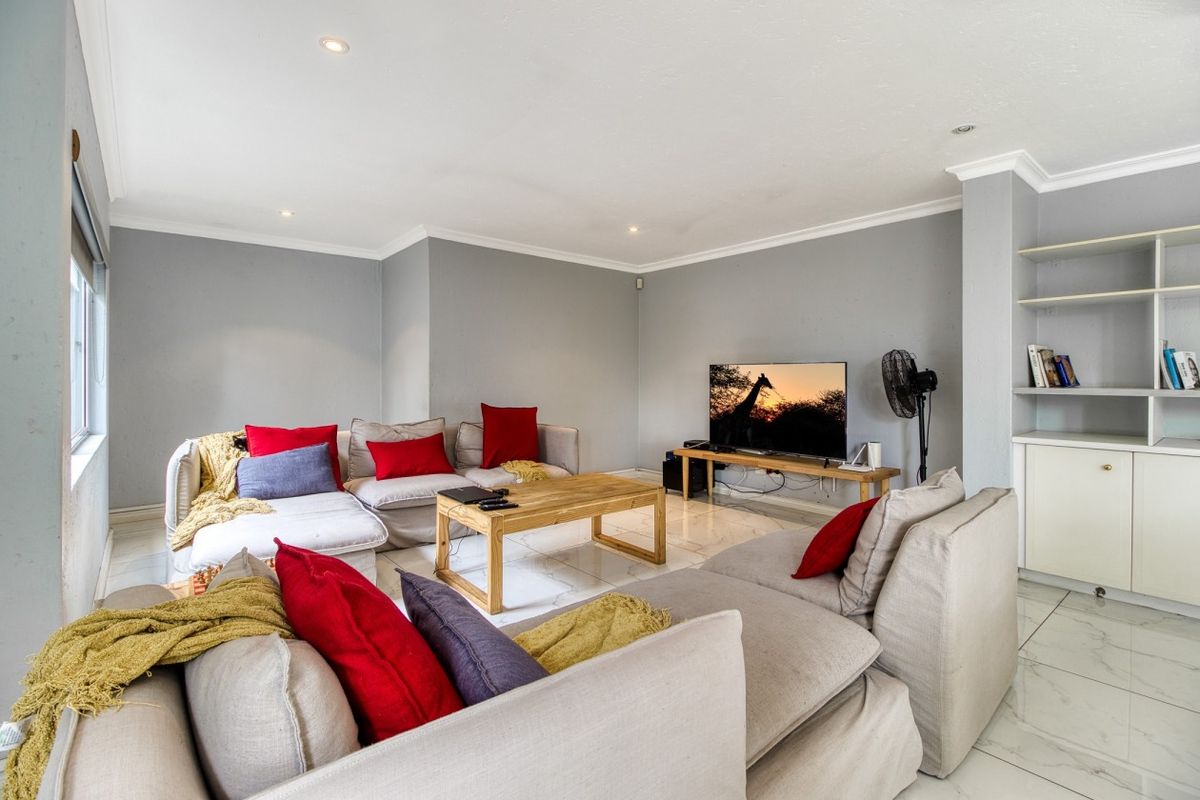 A bright and spacious living room featuring tiled flooring, recessed downlighting, and built-in shelving units.