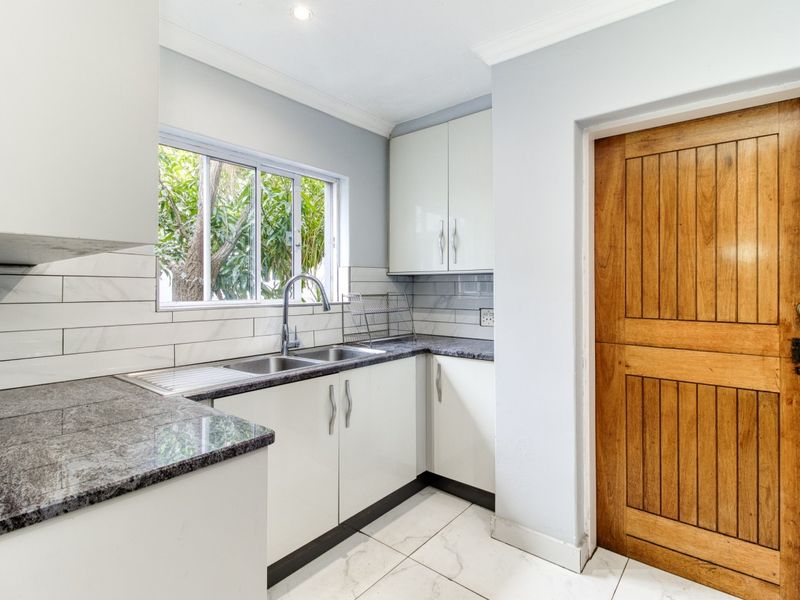 A clean and functional scullery featuring granite countertops, a double basin sink, subway tile backsplash, and ample built-in cabinetry.
