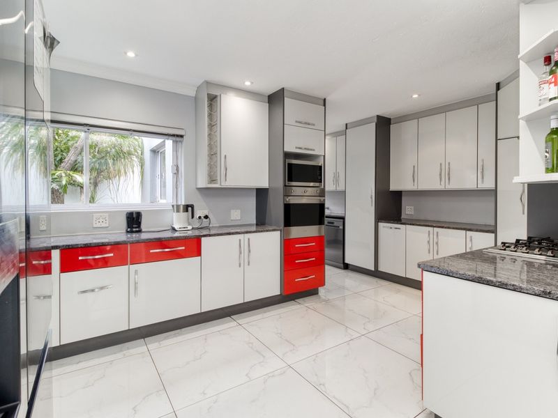 Modern kitchen featuring high-gloss cabinetry, granite countertops, built-in oven and microwave, gas hob, and large format tiled flooring.