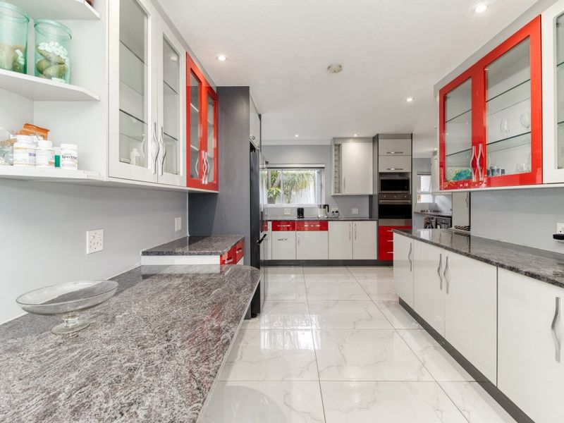 Modern kitchen featuring granite countertops, high-gloss cabinetry with red accents, built-in appliances, and polished tiled flooring.