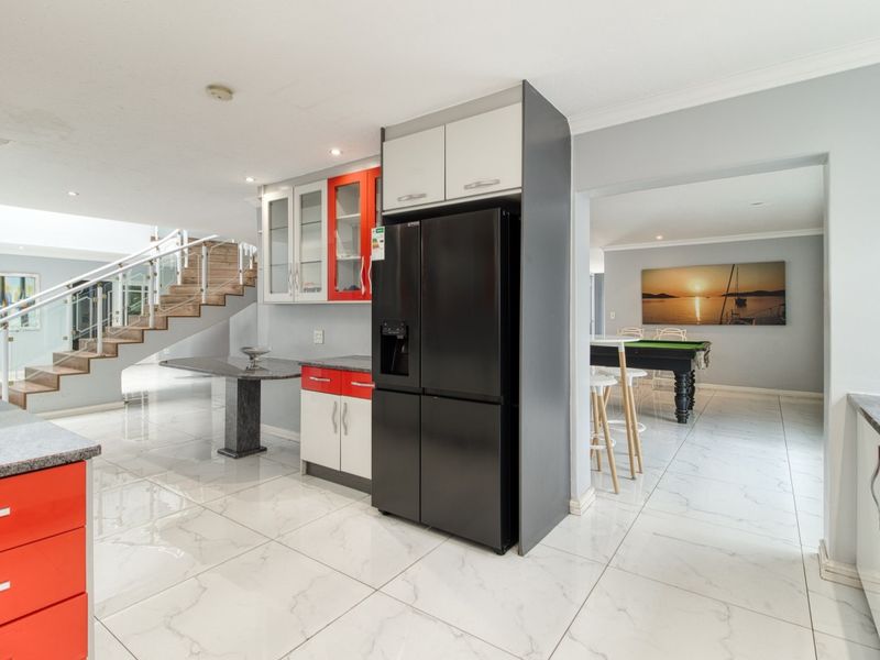 Open-plan kitchen area featuring modern cabinetry, granite countertops, and polished tiled flooring, seamlessly connecting to the staircase and adjacent living space.