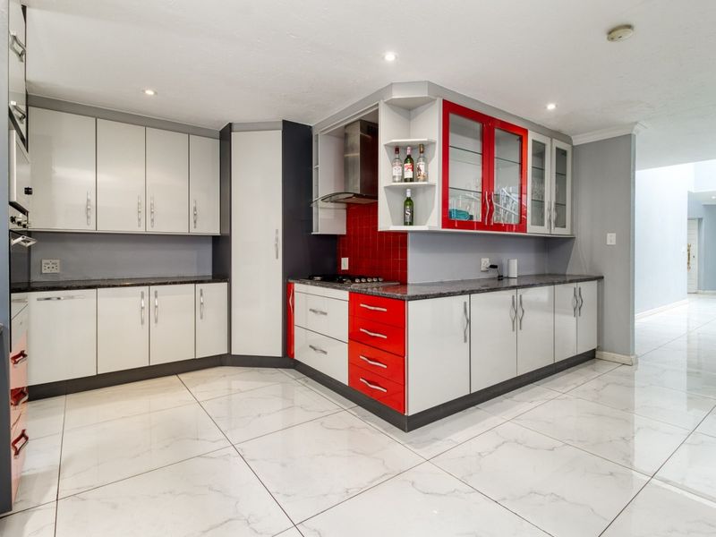Modern kitchen featuring high-gloss cabinetry, granite countertops, a red tiled backsplash, and polished marble-look floor tiles.