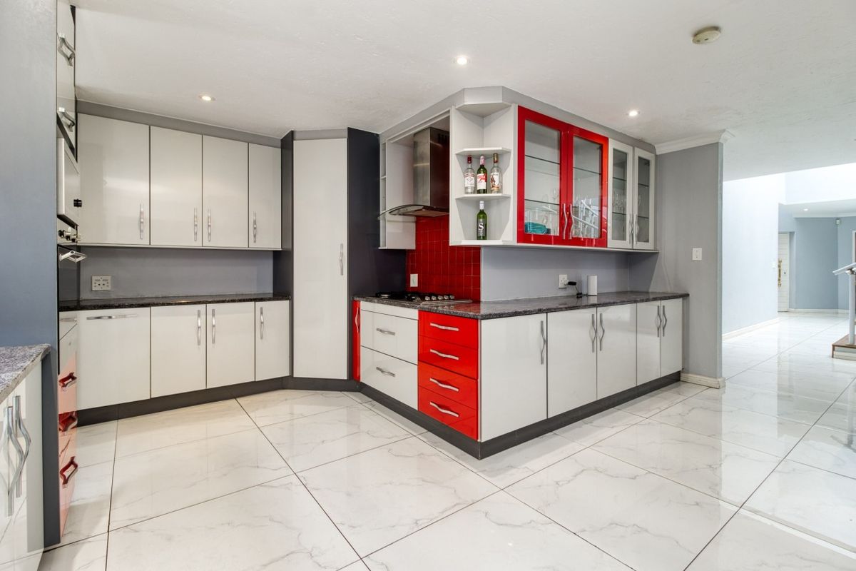 Modern kitchen featuring high-gloss cabinetry, granite countertops, a red tiled backsplash, and polished marble-look floor tiles.