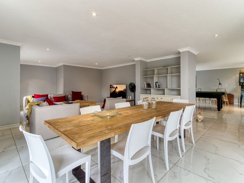 Spacious open-plan living and dining area featuring polished porcelain floor tiles, recessed downlighting, and a custom built-in shelving unit.