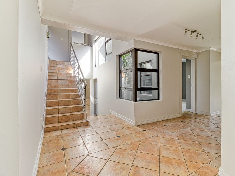Spacious entrance hall featuring ceramic tiled flooring, a staircase with a stainless steel balustrade, and a unique corner window design.