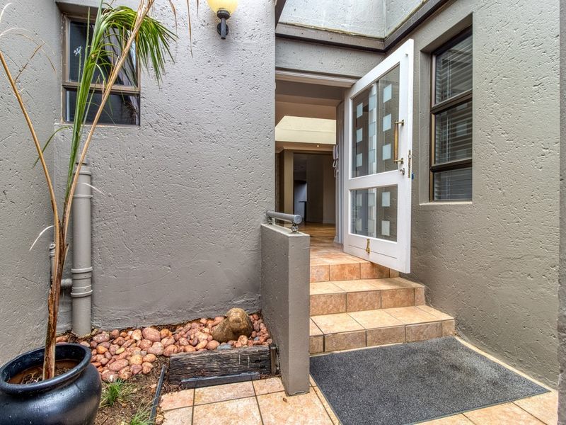 Entrance area featuring tiled steps leading to a glass-panelled front door, set against a textured exterior wall with a small landscaped rock garden.