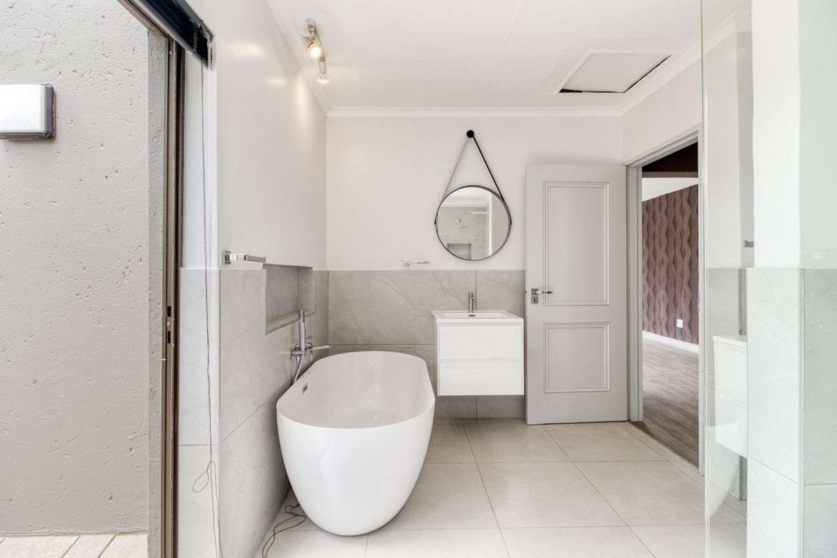 Modern bathroom featuring a sleek freestanding bathtub, wall-mounted vanity, and contemporary grey tiled finishes with clean lines and bright lighting.