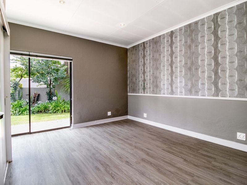 An empty bedroom featuring modern laminate flooring, a decorative wallpaper accent wall, and a sliding glass door providing direct access to the garden.
