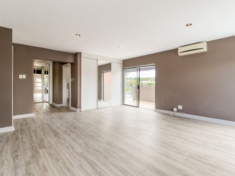 Spacious bedroom featuring laminate flooring, built-in mirrored cupboards, air conditioning, and a sliding door leading to an outdoor balcony.