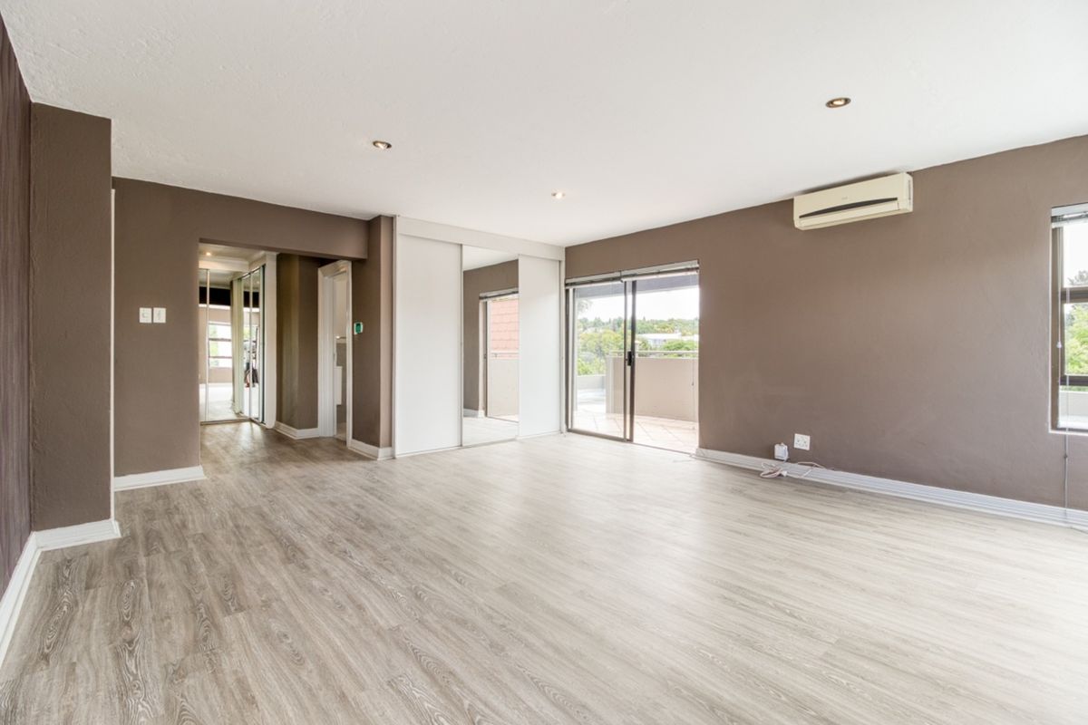 Spacious bedroom featuring laminate flooring, built-in mirrored cupboards, air conditioning, and a sliding door leading to an outdoor balcony.