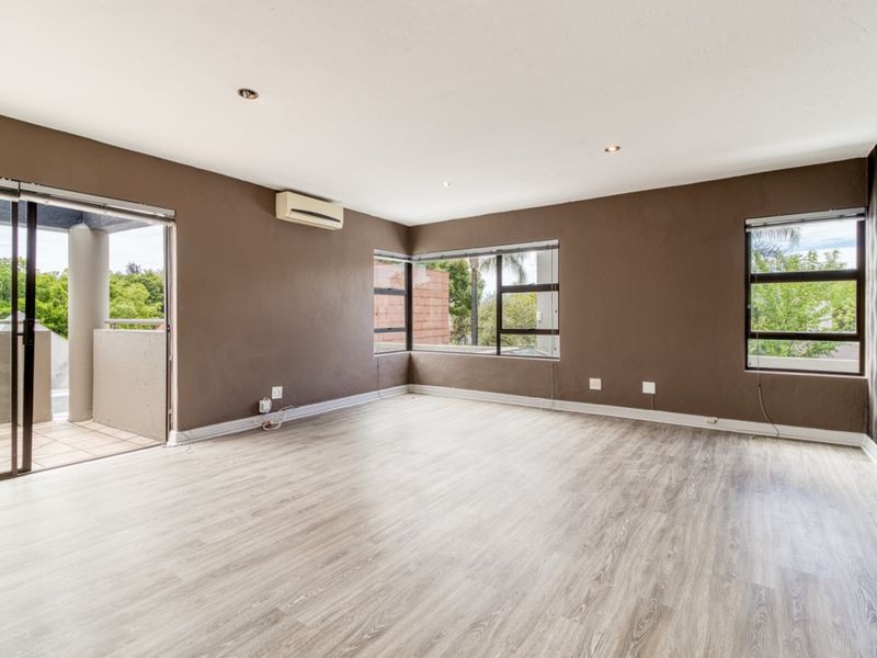Spacious living area featuring laminate flooring, recessed lighting, an air conditioning unit, and direct access to an outdoor balcony through sliding glass doors.