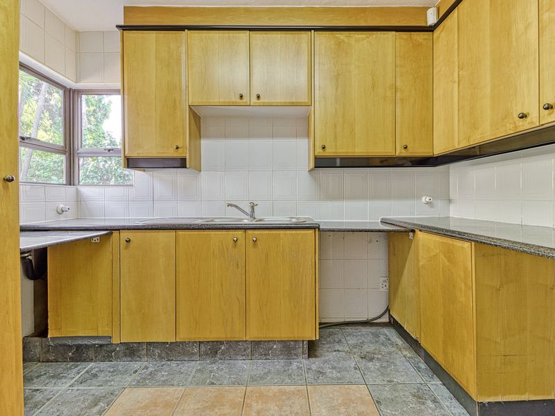 A dated kitchen featuring wooden cabinetry, granite countertops, and tiled flooring. The space is empty and ready for a modern renovation.