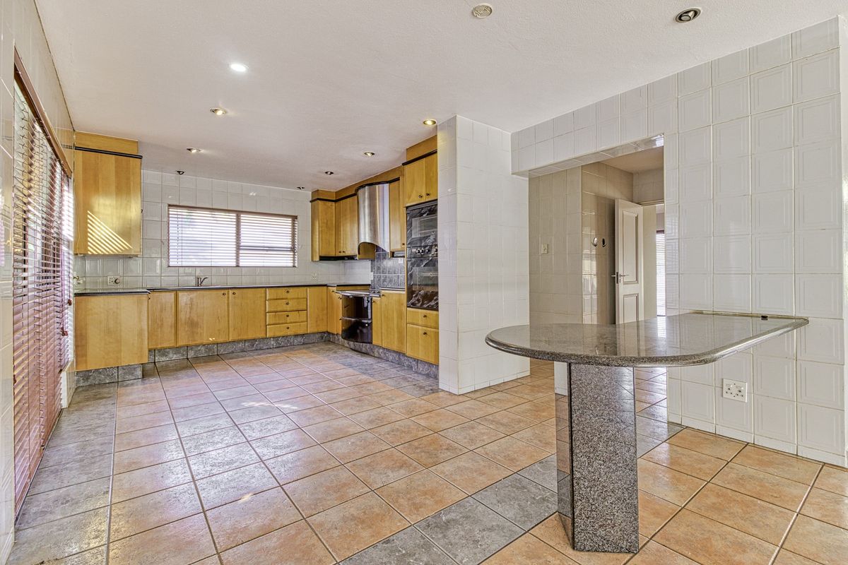 Spacious kitchen featuring wooden cabinetry, granite breakfast bar, tiled flooring, and built-in appliances, offering a functional layout with ample storage space.