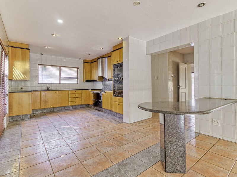 Spacious kitchen featuring wooden cabinetry, granite breakfast bar, tiled flooring, and built-in appliances, offering a functional layout with ample storage space.
