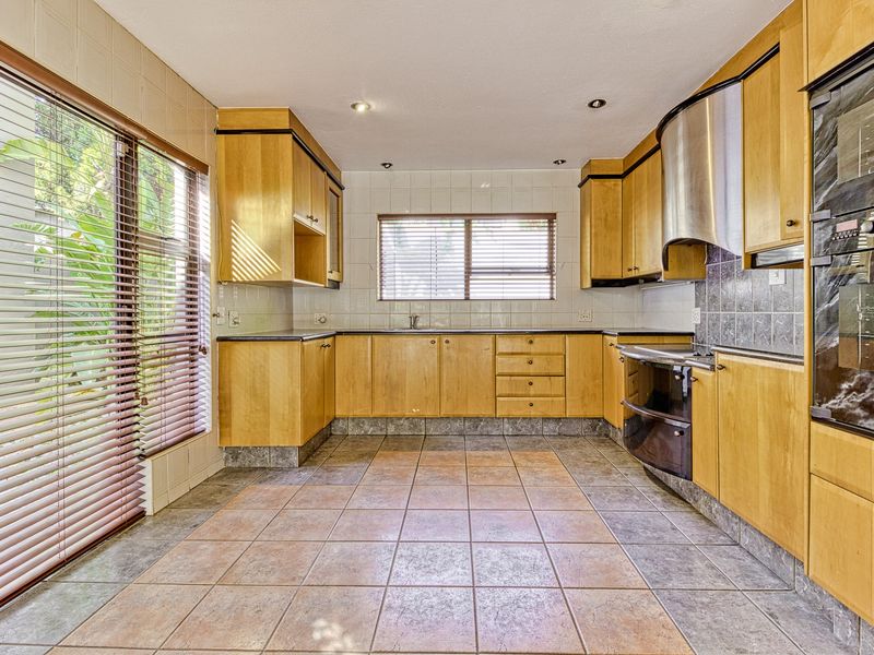 A spacious kitchen featuring light wood cabinetry, tiled flooring, a built-in oven, and a stainless steel extractor fan, with natural light from large windows.