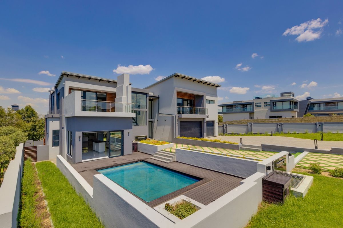 Modern double-story residence featuring a rear swimming pool, timber decking, glass-railed balconies, and a spacious paved driveway with double garage access.