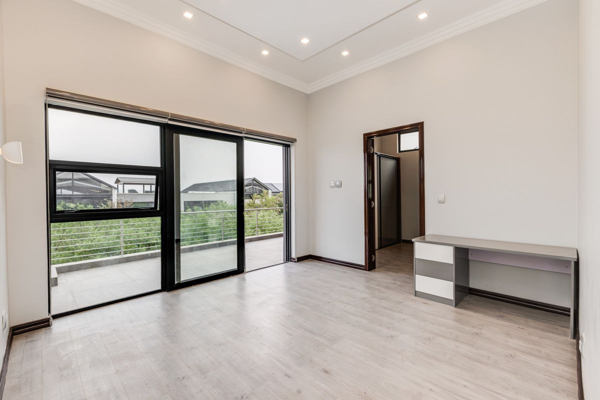 Spacious bedroom featuring light laminate flooring, recessed ceiling lighting, and large sliding glass doors opening onto a private balcony.