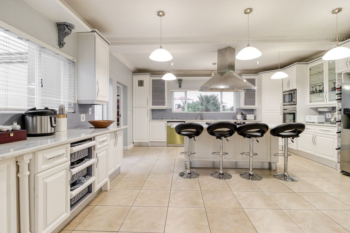 Spacious kitchen featuring a large central island with breakfast bar seating, stainless steel extractor fan, built-in oven, and ample cabinetry.