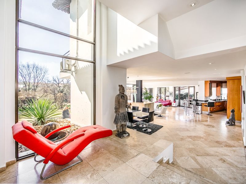 Spacious open-plan living area featuring high ceilings, expansive double-volume windows, travertine flooring, and a modern kitchen with integrated cabinetry.