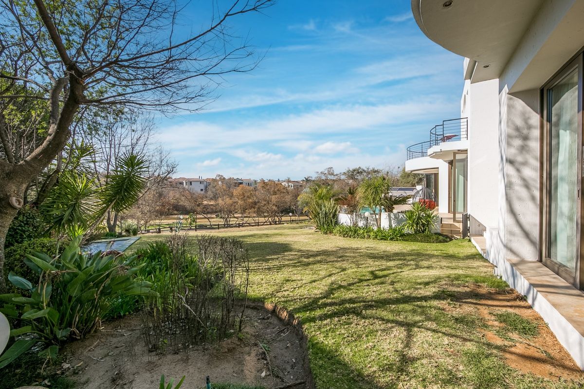 A spacious rear garden featuring a well-maintained lawn, mature landscaping, and a modern building facade with a balcony and large sliding glass doors.