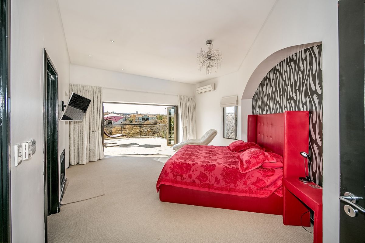 Spacious bedroom featuring an arched feature wall, recessed lighting, and large sliding glass doors opening onto a private balcony with scenic views.