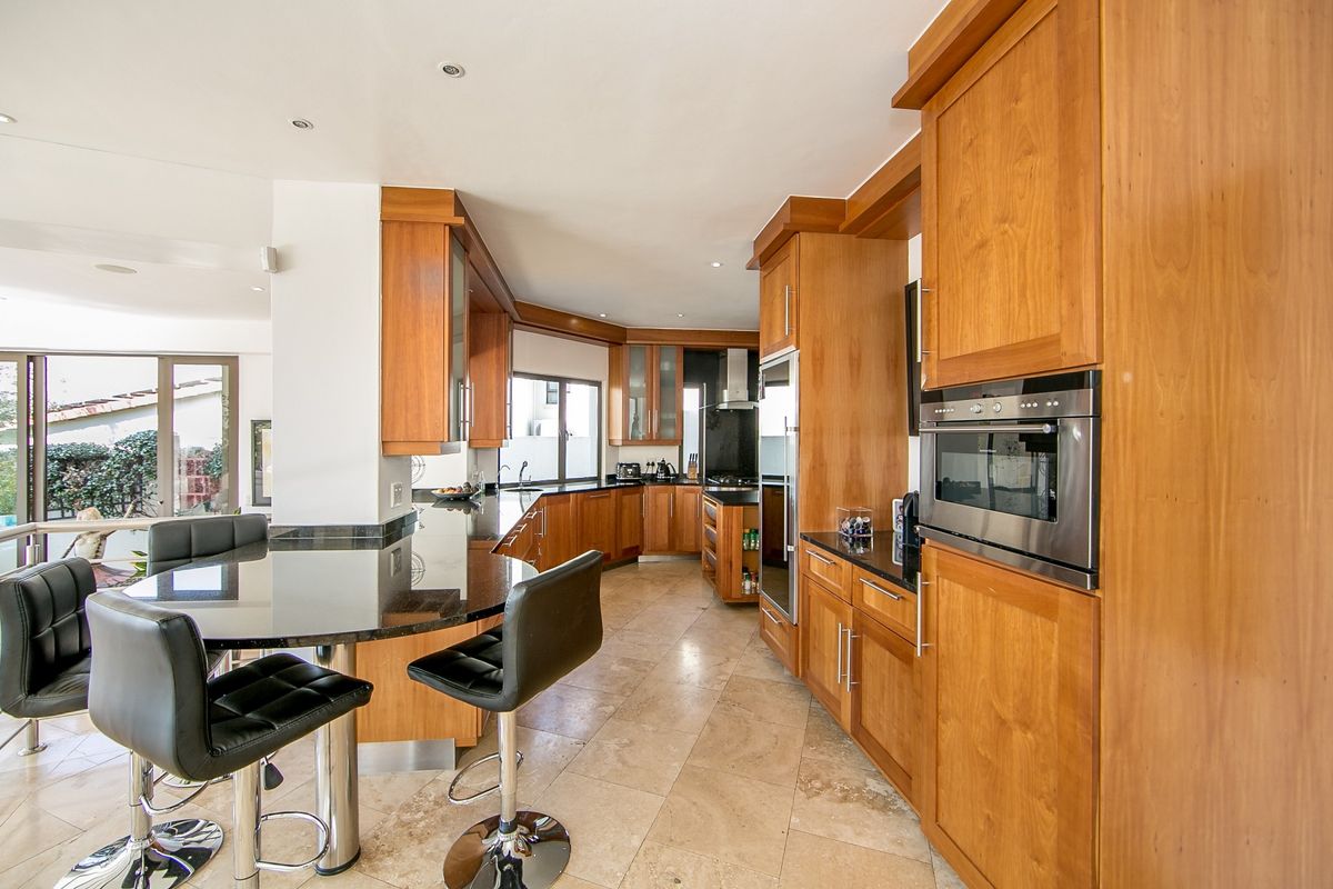 Spacious kitchen featuring warm wooden cabinetry, granite countertops, integrated oven, and stone tile flooring with a breakfast bar area.