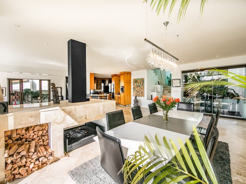 Spacious open-plan living and dining area featuring a central stone-clad fireplace, stone flooring, and seamless flow to the kitchen and outdoor patio.