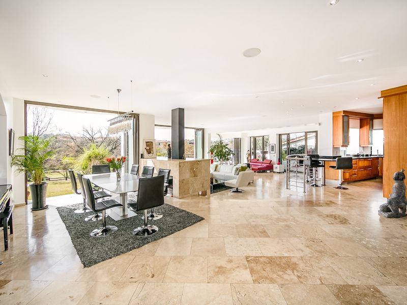 Spacious open-plan living and dining area featuring travertine flooring, a stone-clad fireplace, and a modern kitchen with integrated cabinetry and island.