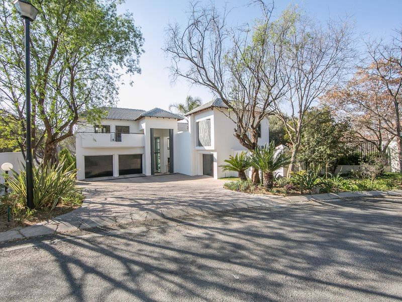 A modern double-story residence featuring a paved driveway, double garage, and a well-maintained front garden with mature trees.