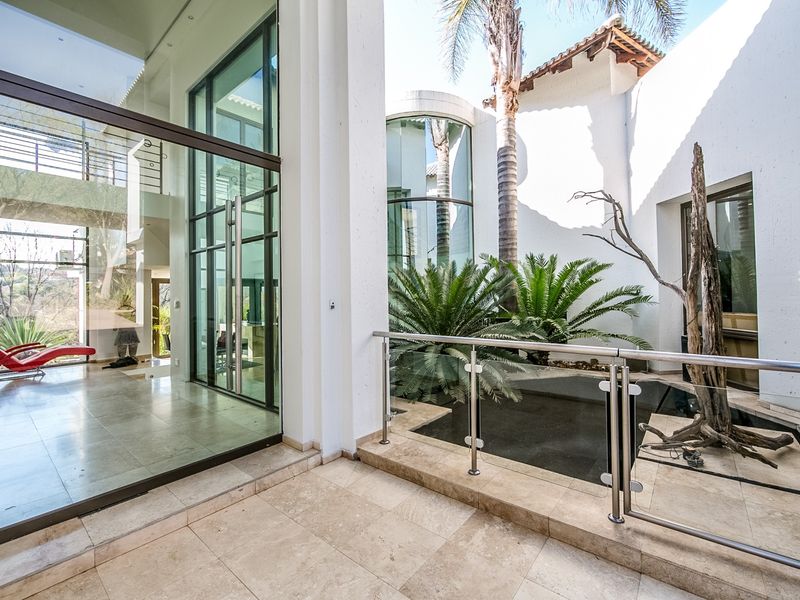 A modern covered patio featuring travertine flooring, a sleek stainless steel and glass balustrade, and a tranquil water feature overlooking the garden.