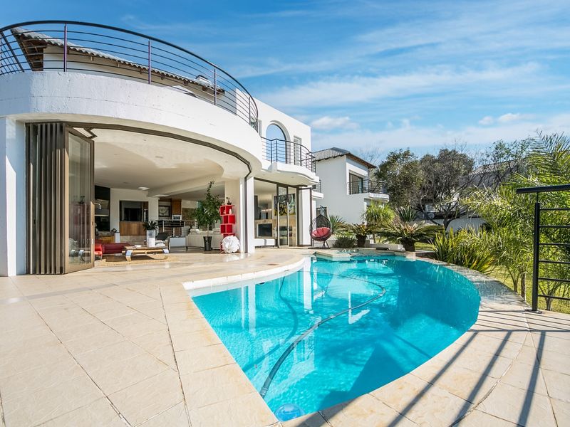A spacious outdoor entertainment area featuring a curved swimming pool, tiled patio, and seamless indoor-outdoor flow through large bi-fold doors.