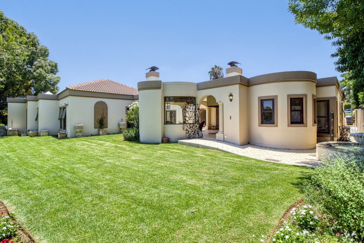A well-maintained rear exterior view of the house featuring a curved architectural design, a paved patio area, and a manicured lawn.