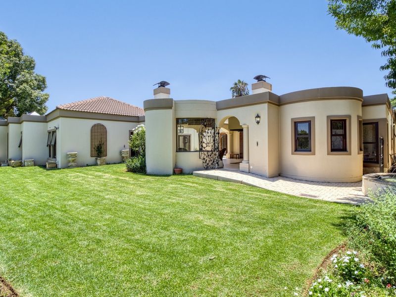 A well-maintained rear exterior view of the house featuring a curved architectural design, a paved patio area, and a manicured lawn.