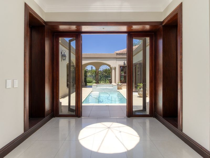 Elegant entrance hall featuring polished tile flooring and grand wooden door frames, opening directly onto a private courtyard with a swimming pool.