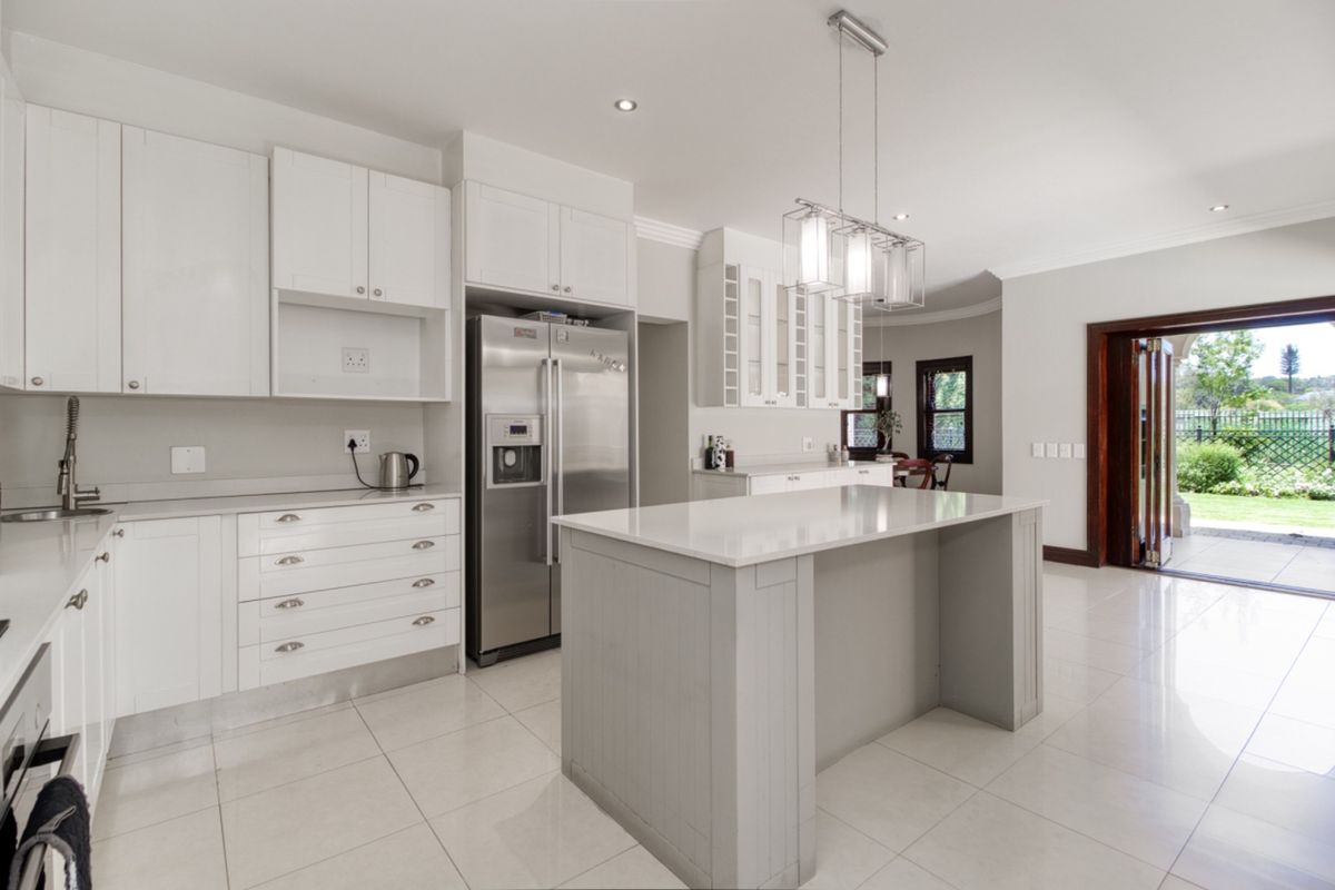 Modern kitchen featuring white cabinetry, a central island with stone countertops, tiled flooring, and direct access to the rear garden through glass doors.