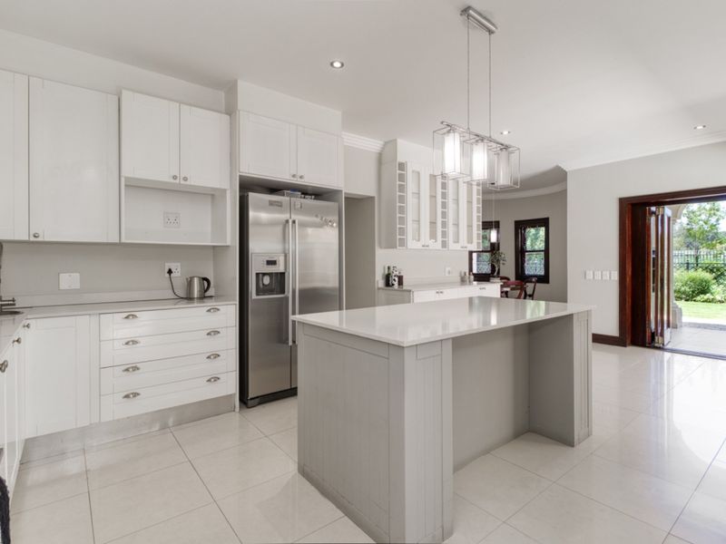 Modern kitchen featuring white cabinetry, a central island with stone countertops, tiled flooring, and direct access to the rear garden through glass doors.