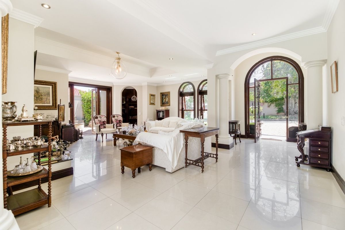 Spacious living room featuring polished tiled flooring, elegant arched doorways with decorative columns, and abundant natural light through arched windows and glass entry doors.