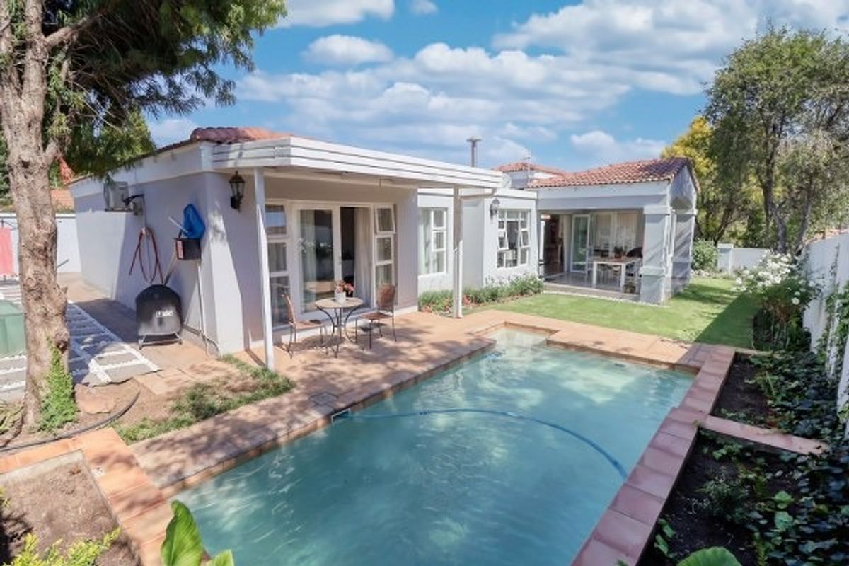 Rear view of the property featuring a swimming pool, covered patio area, and well-maintained garden with established trees.