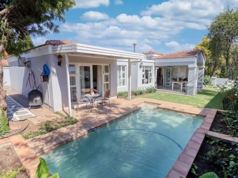 Rear view of the property featuring a swimming pool, covered patio area, and well-maintained garden with established trees.