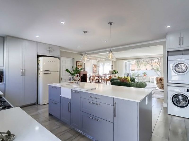Modern open-plan kitchen featuring a central island with quartz countertops, farmhouse sink, integrated cabinetry, and dedicated laundry area with stacked appliances.