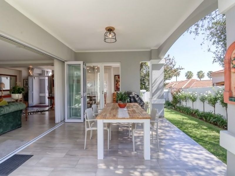 A spacious covered patio featuring large-format floor tiles and seamless folding glass doors that open into the main living area, overlooking a manicured garden.