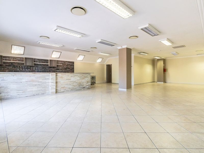 Spacious open-plan office area featuring a built-in reception counter, stone and brick accents, tiled flooring, and recessed fluorescent lighting throughout.